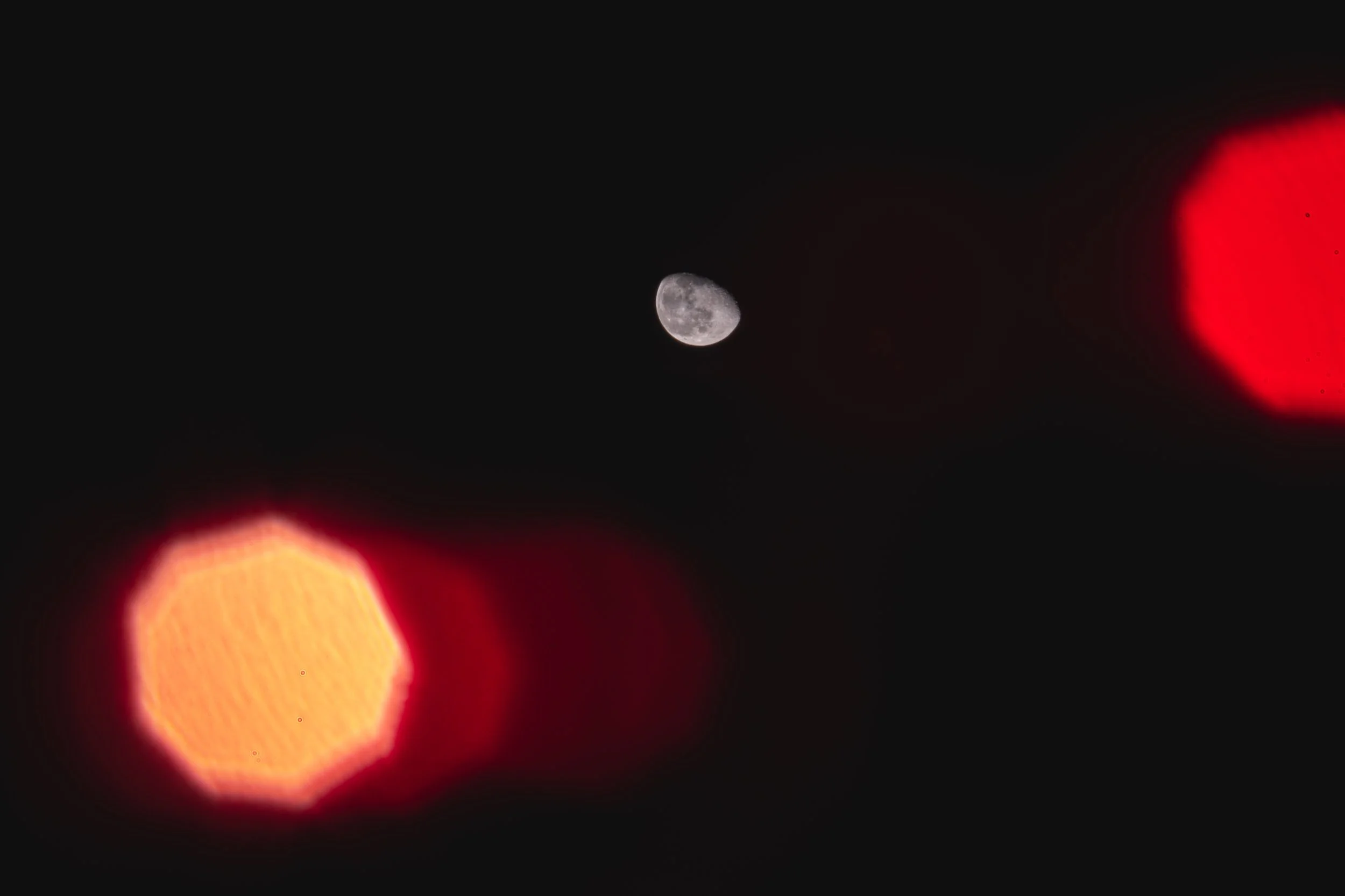 A visible moon in the night sky with bright red and orange lens flares likely from a nearby light source.