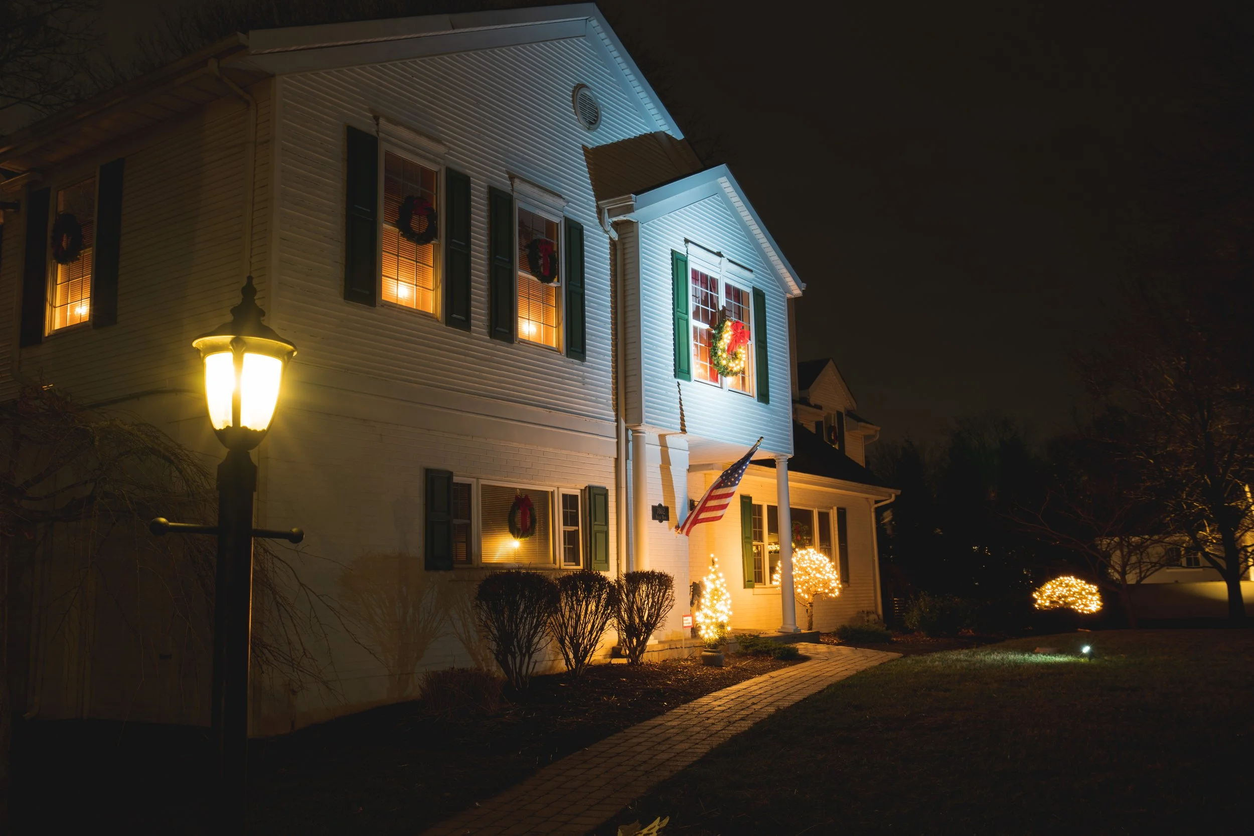 A house decorated with Christmas lights and wreaths, illuminated at night, with an American flag near the entrance.
