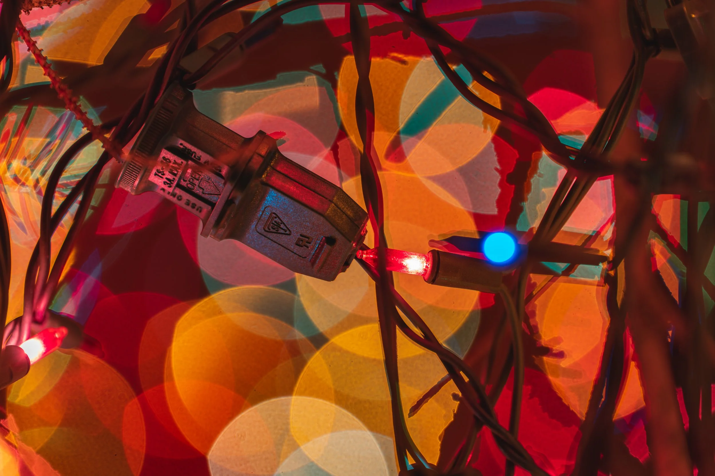 Close-up of tangled multicolored Christmas lights with blurred colorful background, one blue and one red bulb lit.