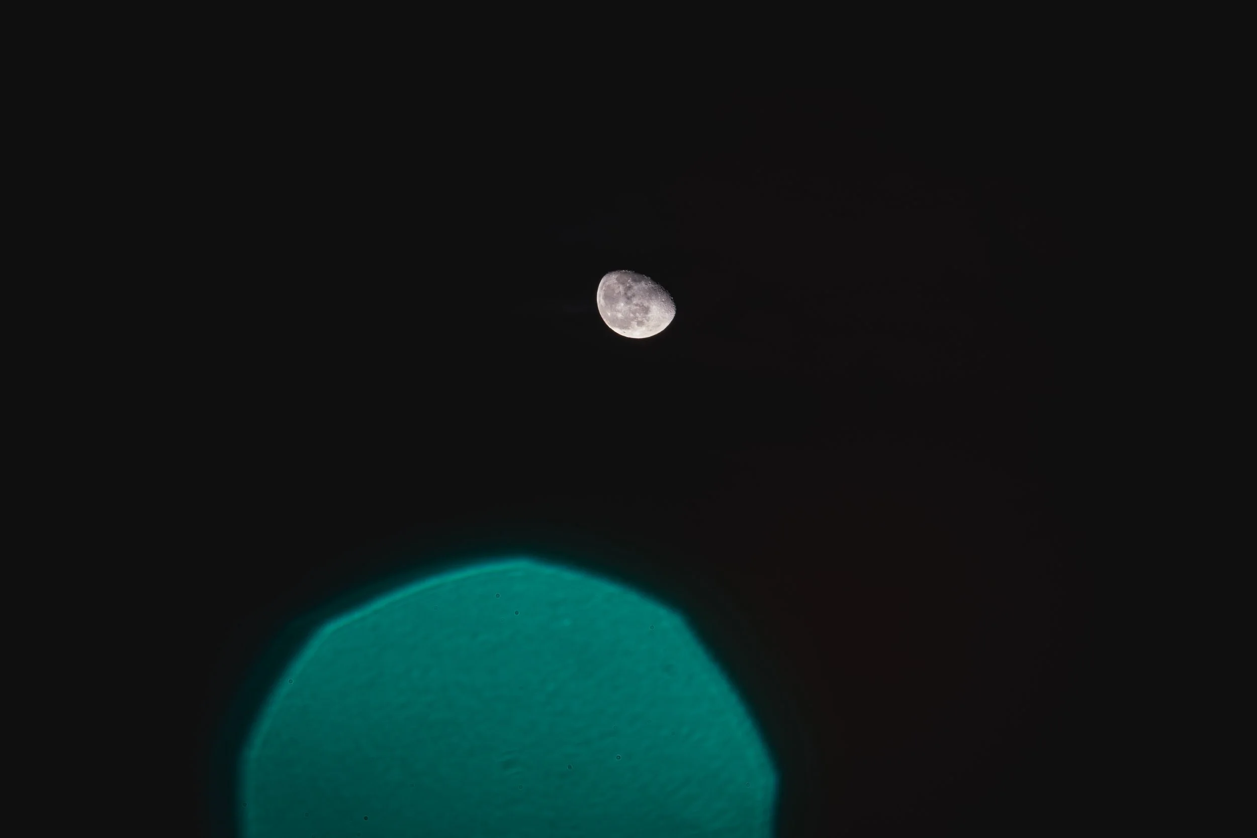 Photo showing the moon in the night sky and a glowing turquoise object below.