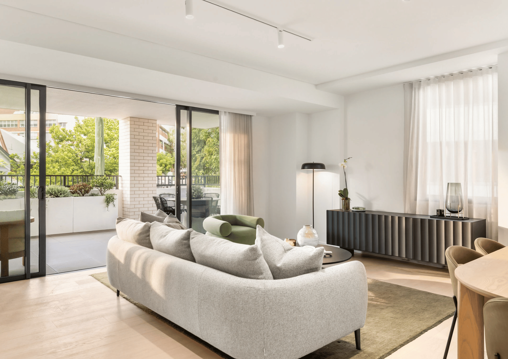 Modern living room with large glass sliding doors leading to a balcony, featuring outdoor patio furniture and potted plants