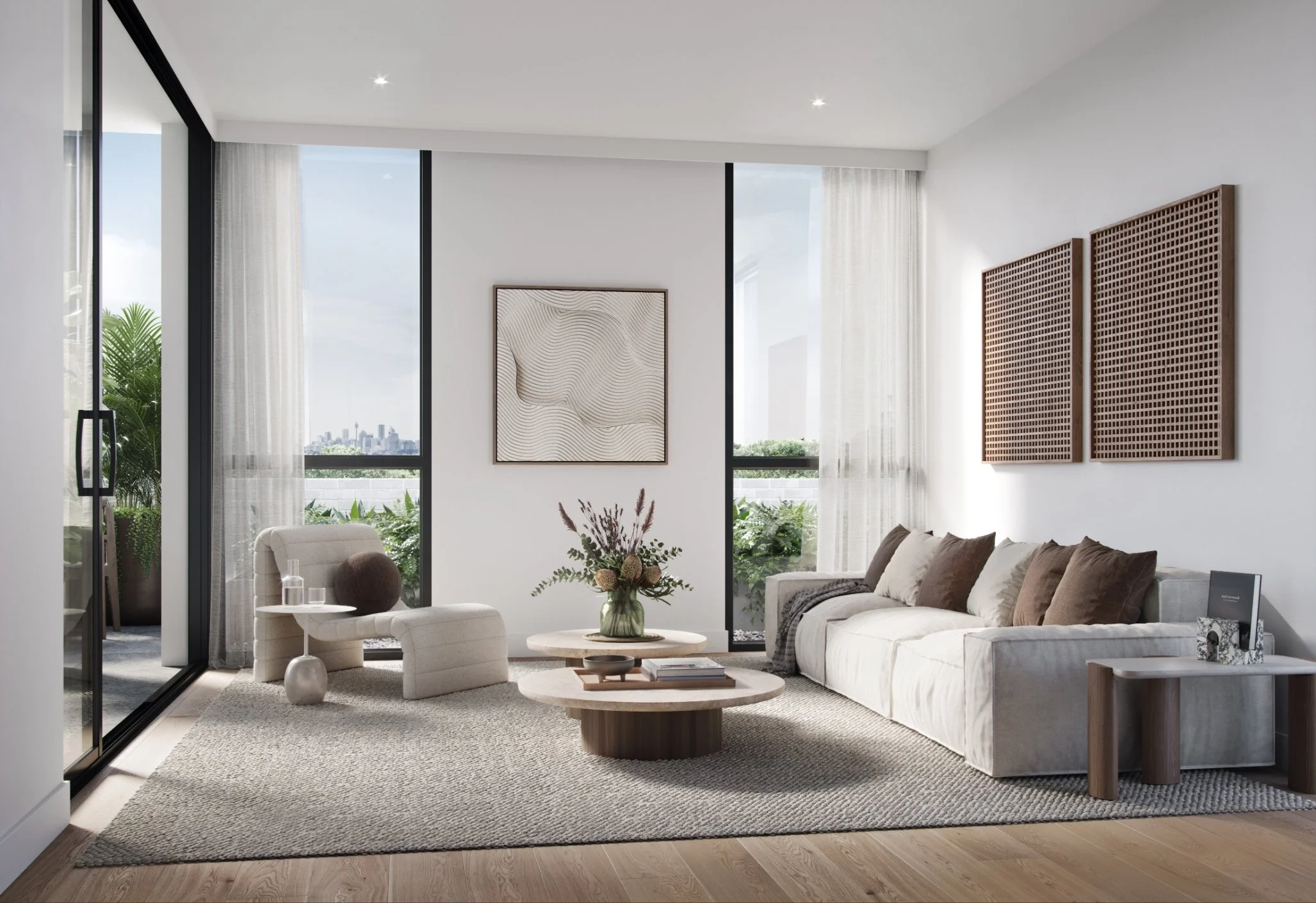 Modern living room with large windows, white walls, abstract art, a white sofa with colorful pillows, a round coffee table with a flower arrangement, a beige armchair with a throw pillow, and natural light flooding in.