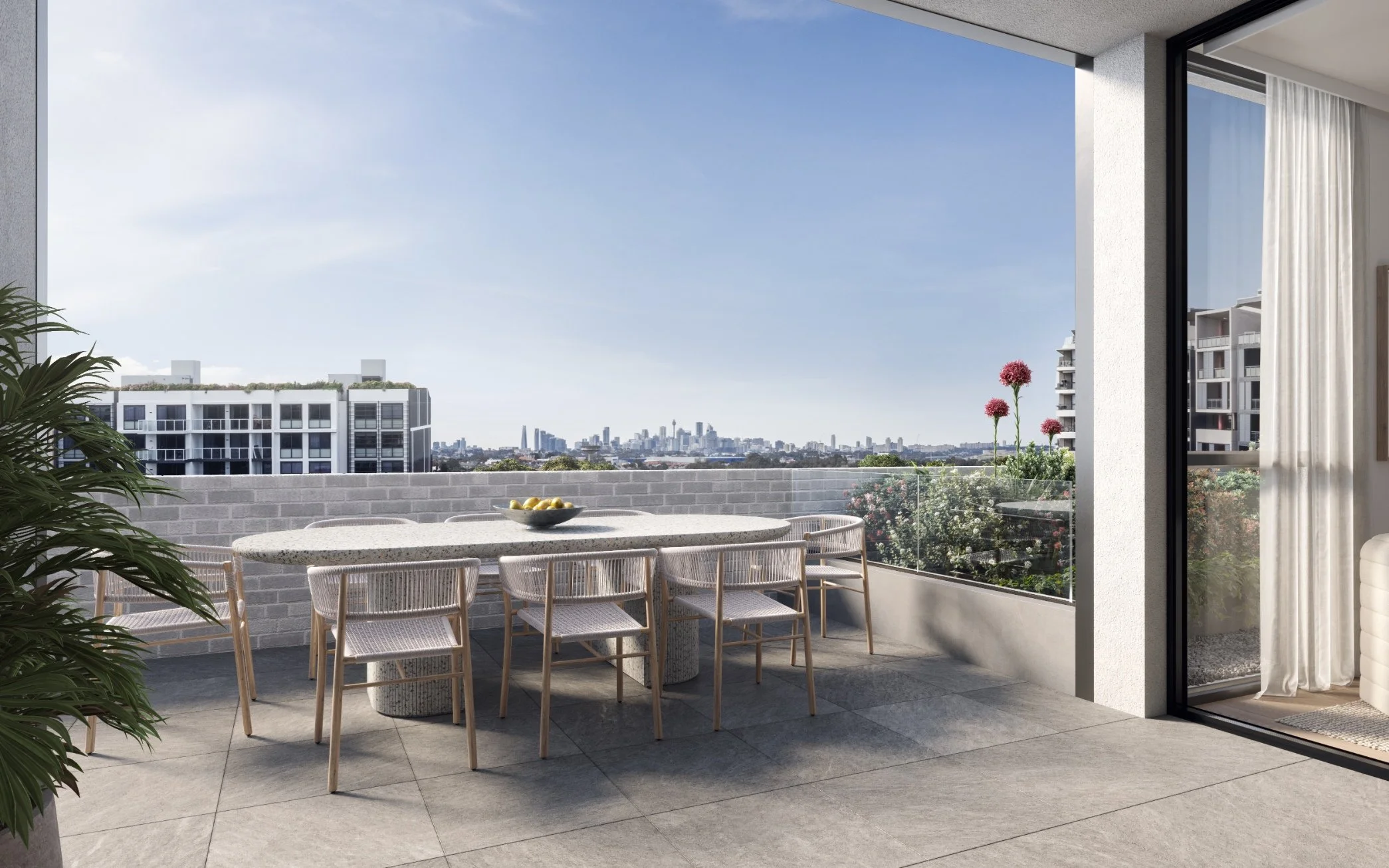 Modern apartment balcony with outdoor dining table and chairs, overlooking city skyline, with pink flowers and potted plant.