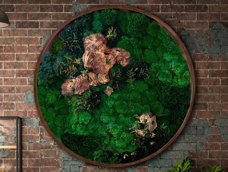 Circular wall art featuring lush green preserved moss and small rocks, mounted on a brick wall.