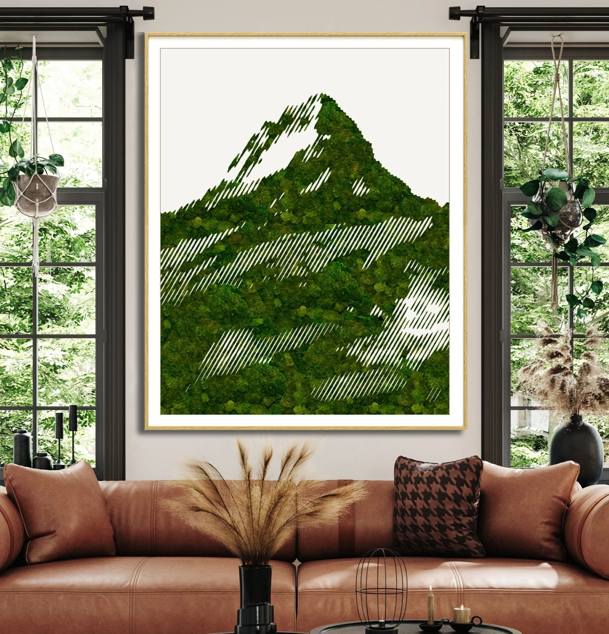 Living room with a large framed moss wall artwork of a mountain with trees on the wall between two windows, with plants hanging on the windows, a tan couch with pillows, and a coffee table with candles and decorative items.