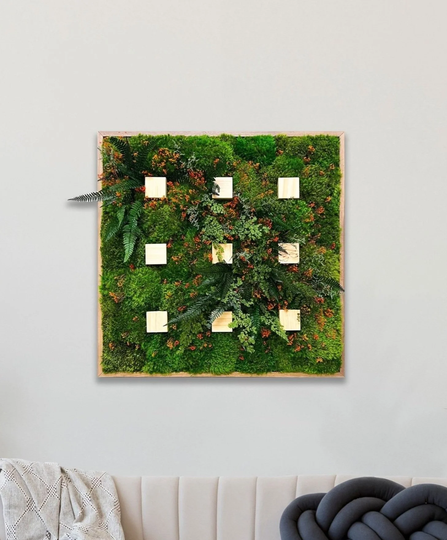 Photo of a framed vertical garden wall with lush green moss and small wooden shelves, mounted on a light-colored wall in a modern interior.