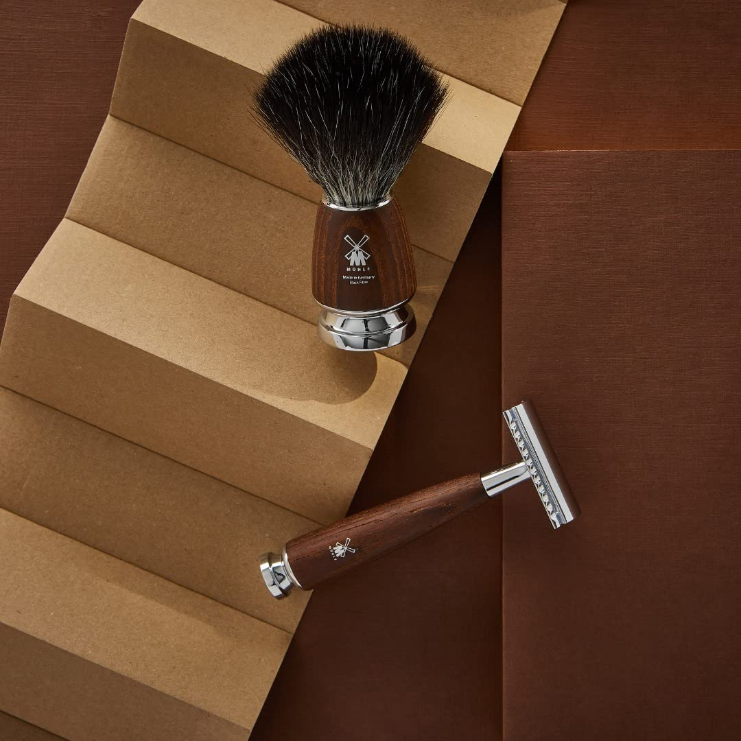 Shaving brush and safety razor with wooden handles on a textured brown background.