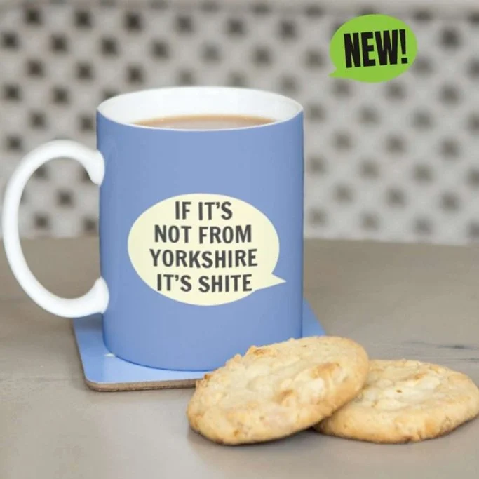 Blue mug with text 'If it's not from Yorkshire it's shite' next to two cookies.