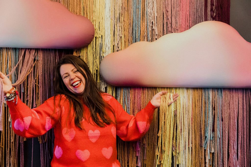 Sara Maxwell stands in front of a wall with colourful clouds