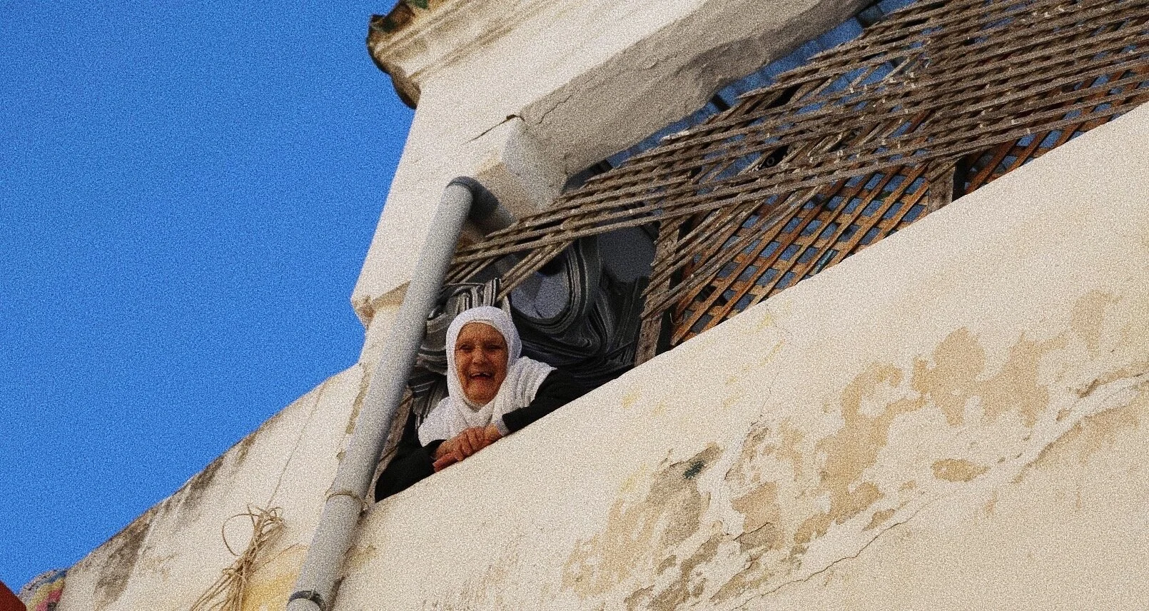 Nun looking down from a balcony with a blue sky background.