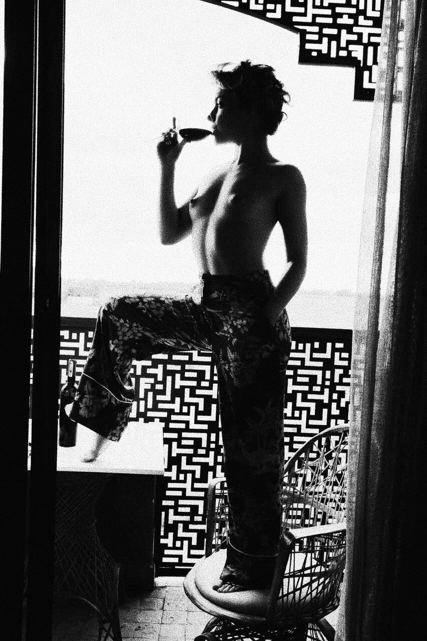 Silhouette of a person with short hair, standing on a chair, posed against a patterned background, holding a wine glass.