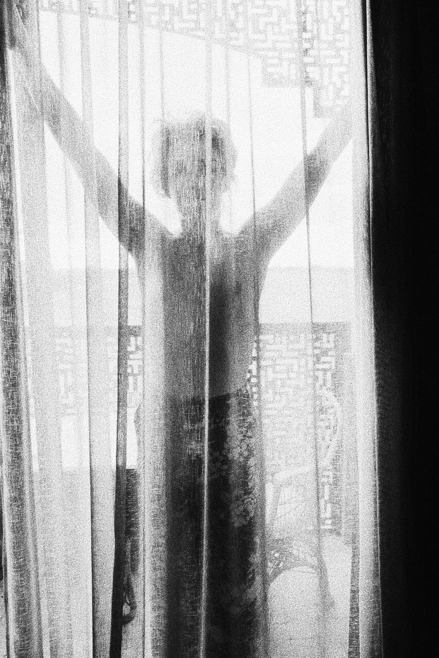 Silhouette of a person standing behind sheer curtains in a black and white setting.