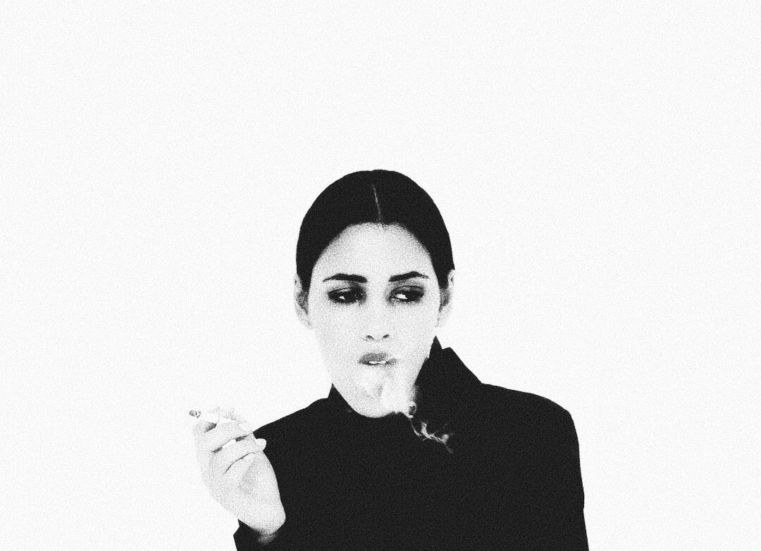 Black and white image of a person with dark hair smoking a cigarette against a white background.