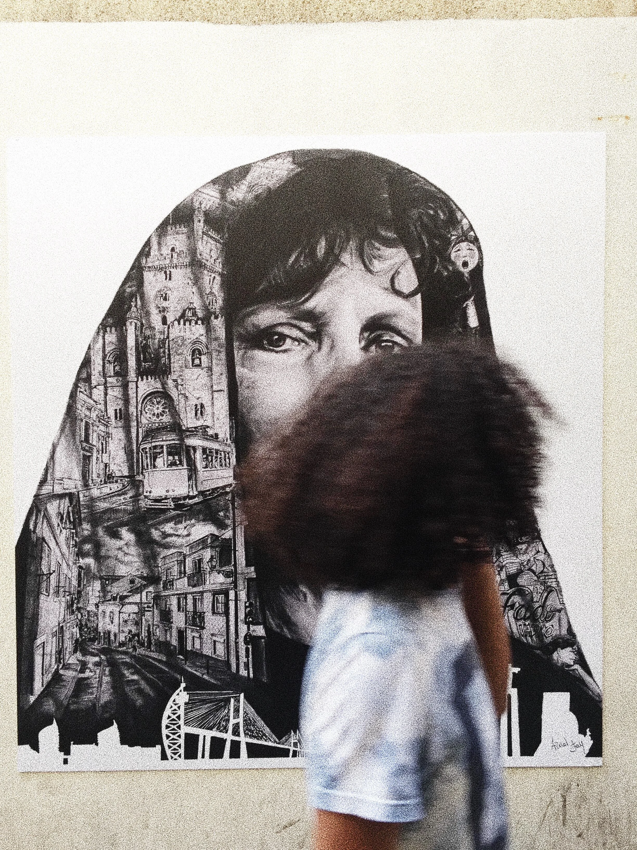 Artwork of a face merged with urban scenes on a wall, person walking by, blurry, curly hair, casual clothing.