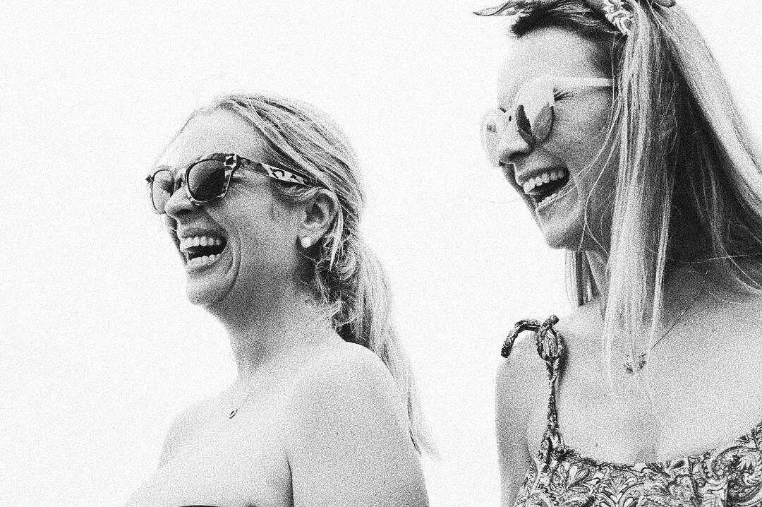 Two women laughing, wearing sunglasses, black and white filter