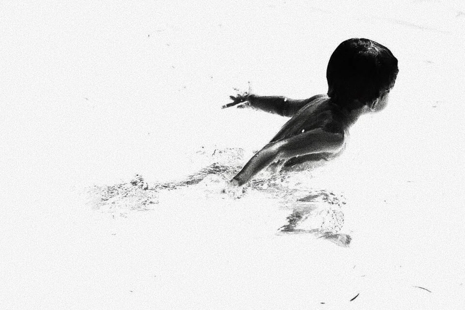 Black and white image of a person swimming in water, with outstretched arms and visible ripples around them.