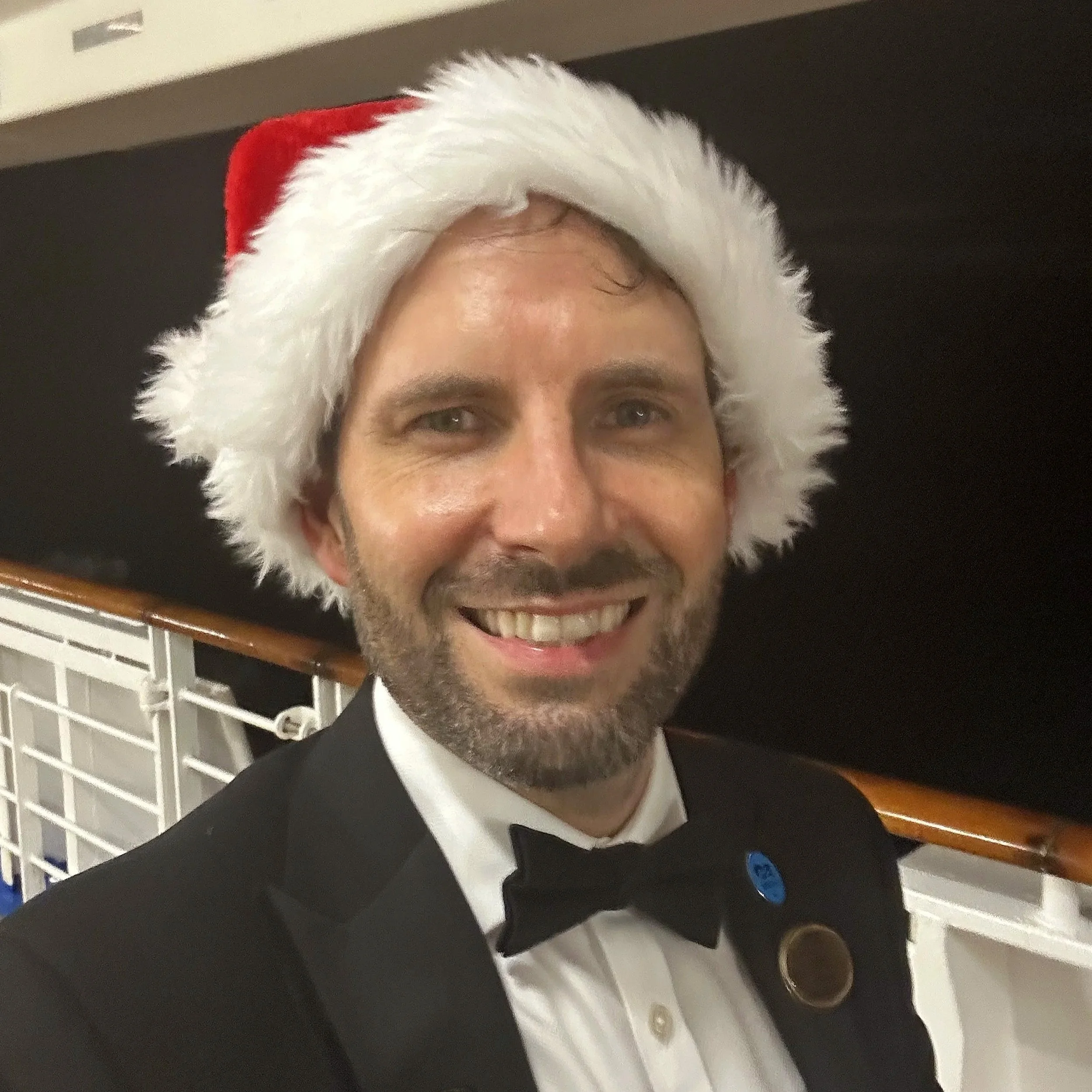 Ian Frost wearing a tuxedo and a Santa hat on the cruise ship decking at night
