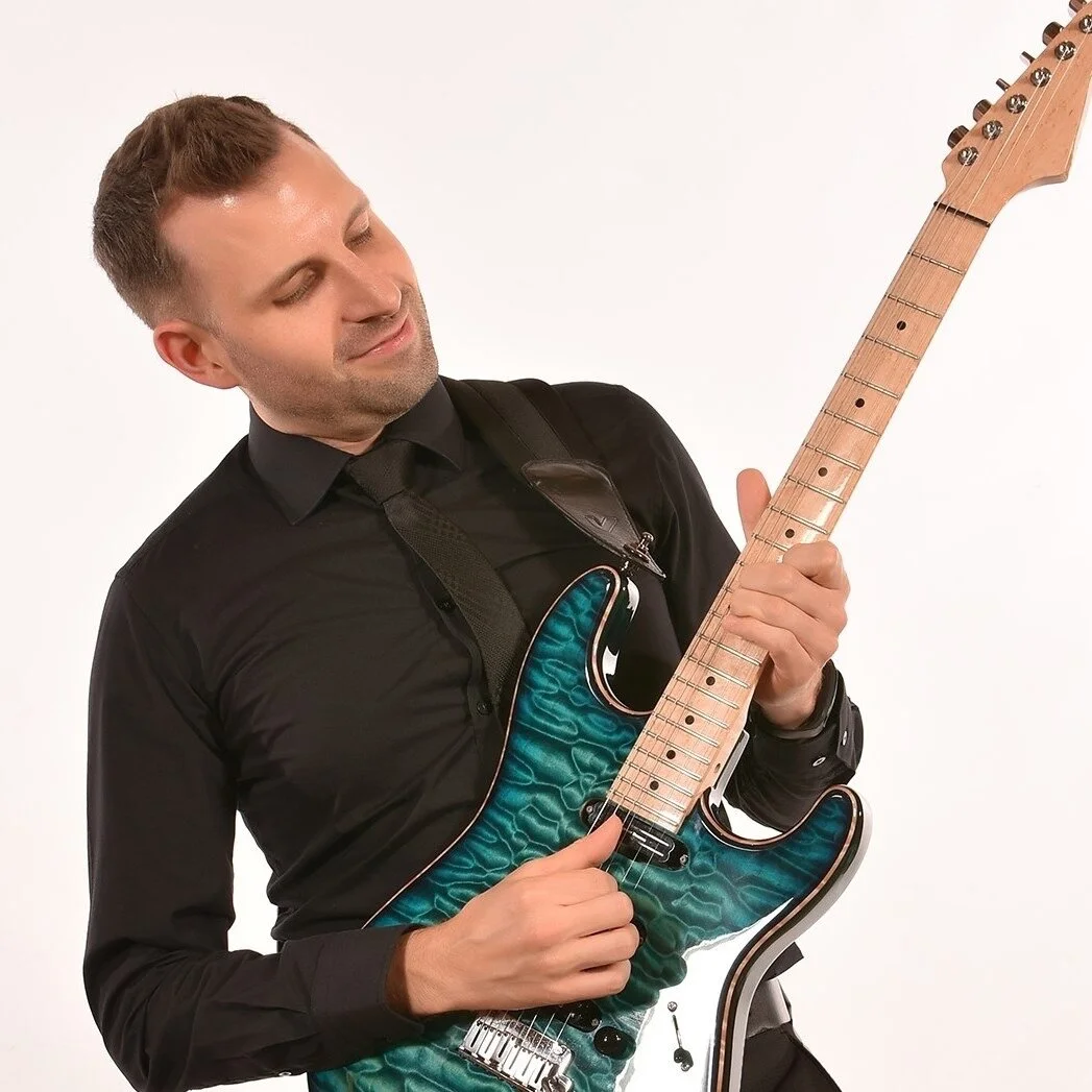 Man playing an electric guitar with a blue quilted pattern and a wooden neck against a plain white background.