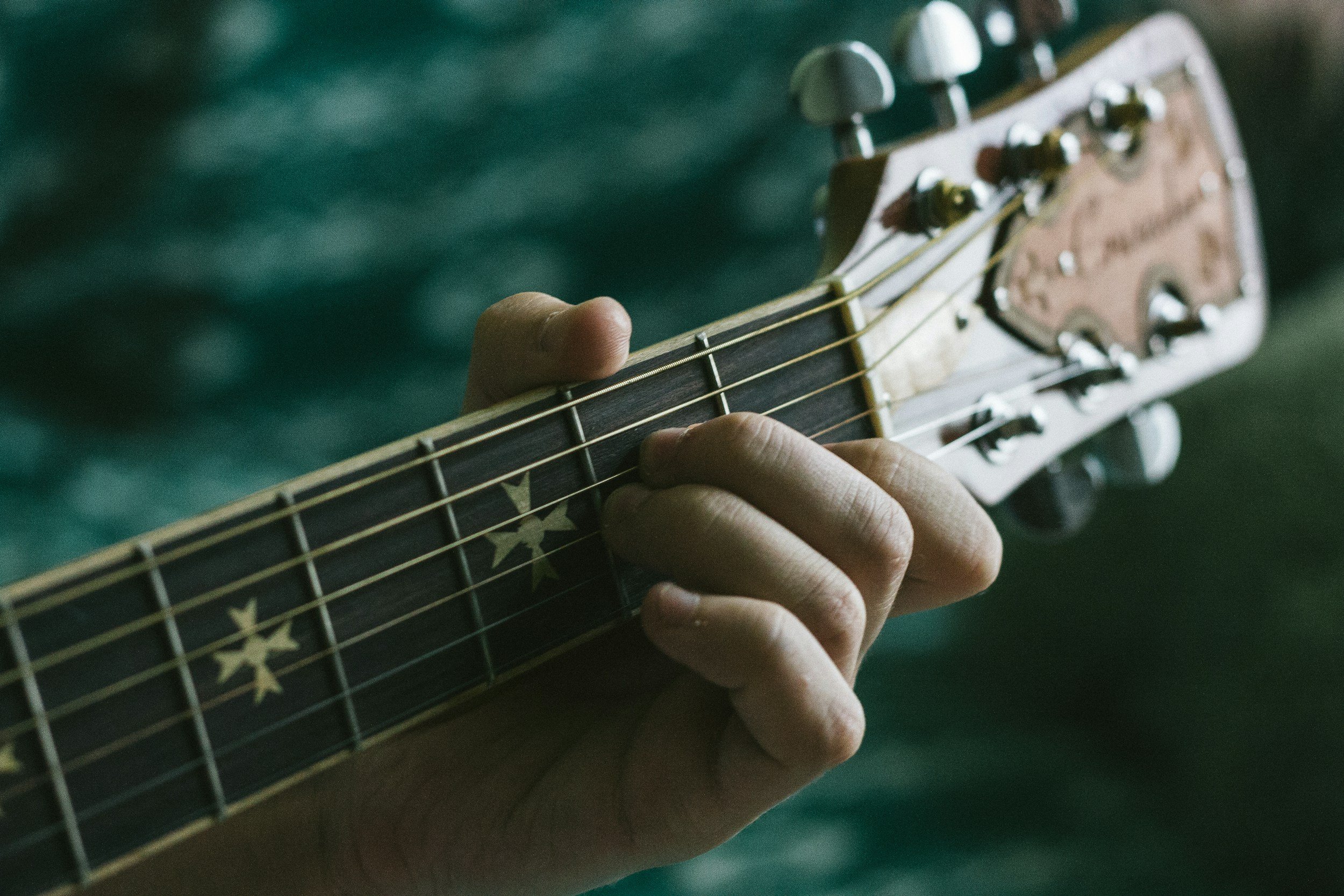 Close-up of a person's hand playing a guitar with star patterns on the fretboard.