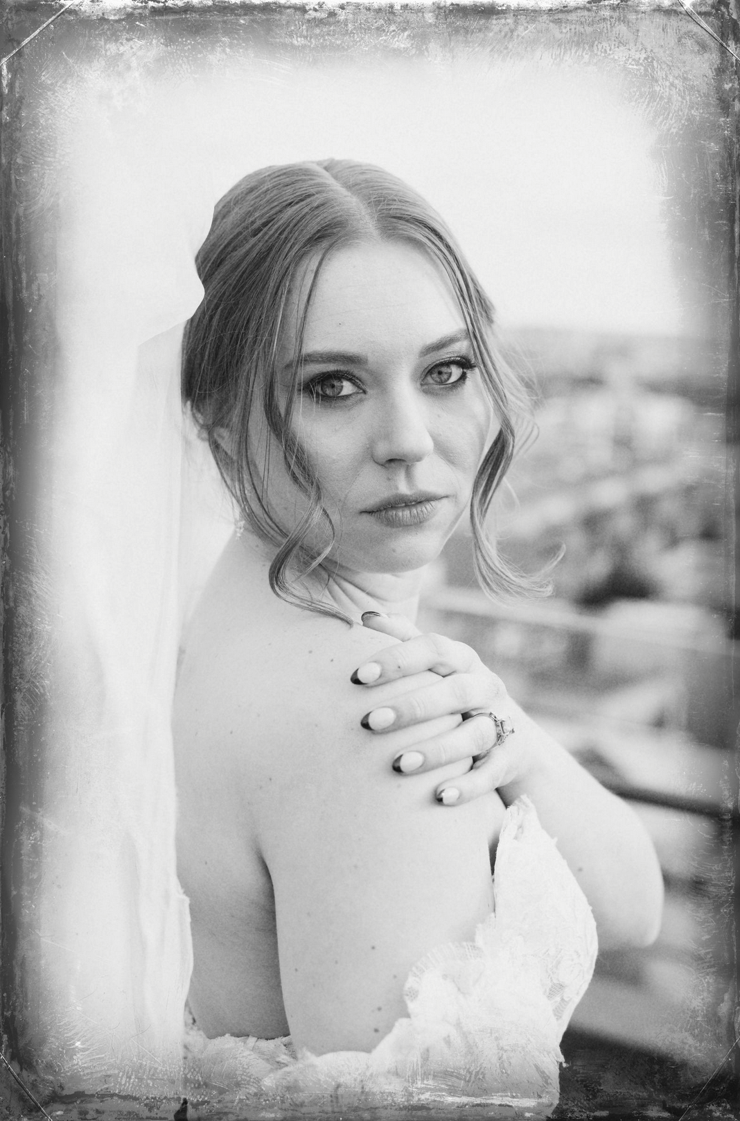 Black and white portrait of a woman with styled hair, wearing a lace off-shoulder dress, with her left hand touching her shoulder, looking directly at the camera, taken by J. Bellocq, luxury wedding photojournalist of Bellocq Weddings in New Orleans.