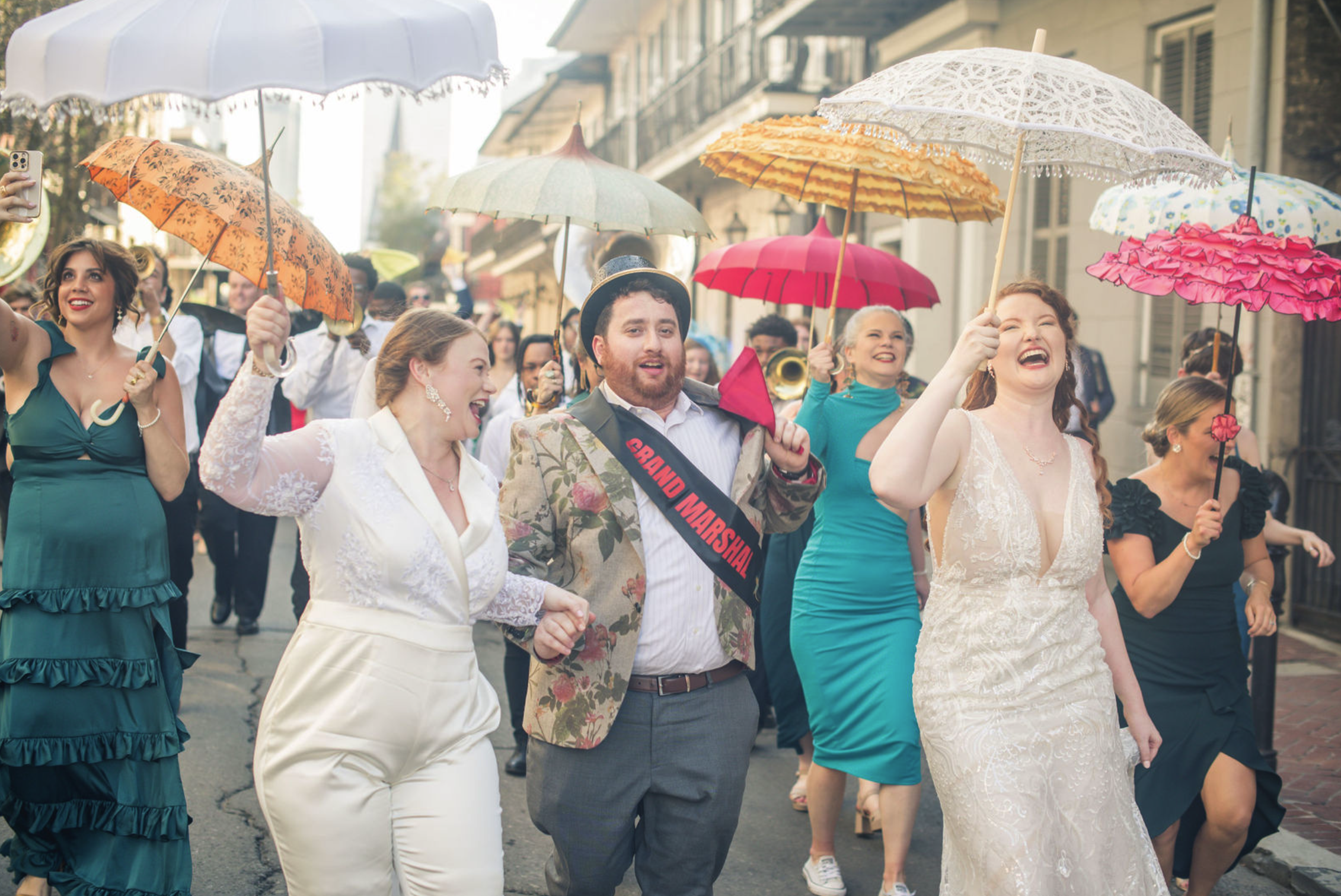 People celebrating in a parade, holding colorful umbrellas and dancing on a city street.