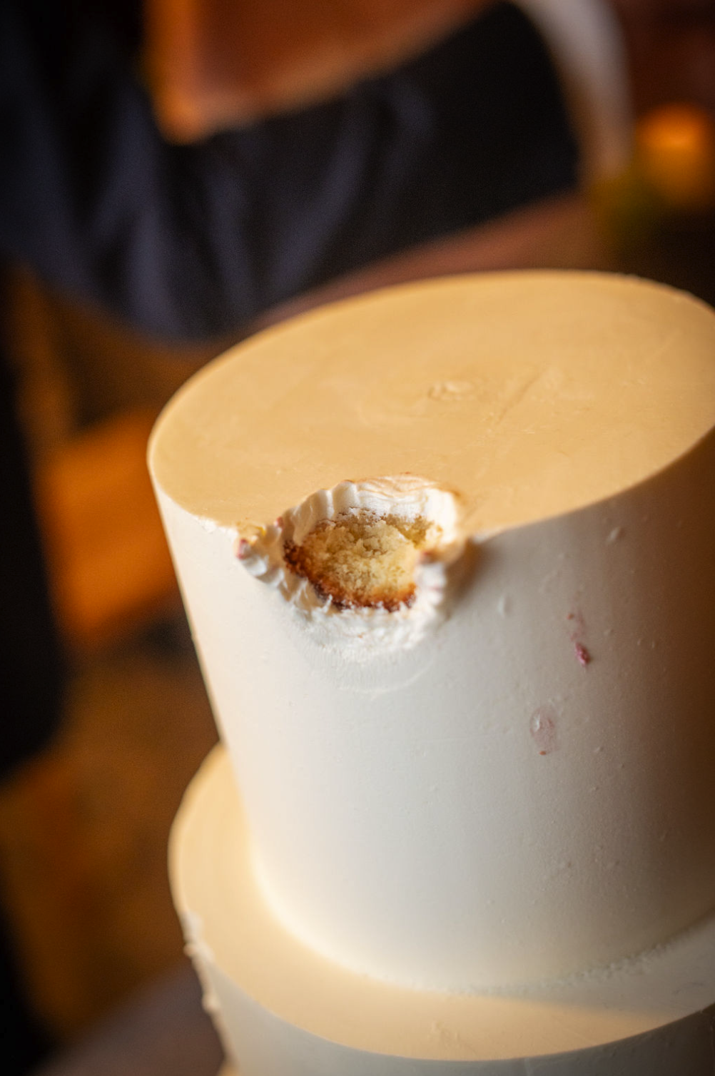 Close-up of a white, three-tiered cake with a smooth finish, featuring a small bite taken out of the top tier.