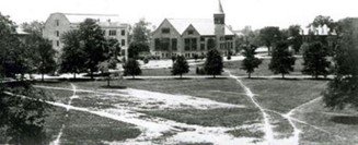 Black and white image of a college campus with a church building, trees, and worn pathways on a grassy area.