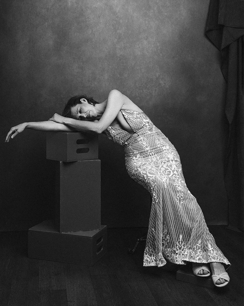 Melanie's portraits are not particularly interested in being beautiful.
They are interested in character.
In the tension between concealment and revelation. Between the theatricality of a long evening dress and the simplicity of bare feet. Between th