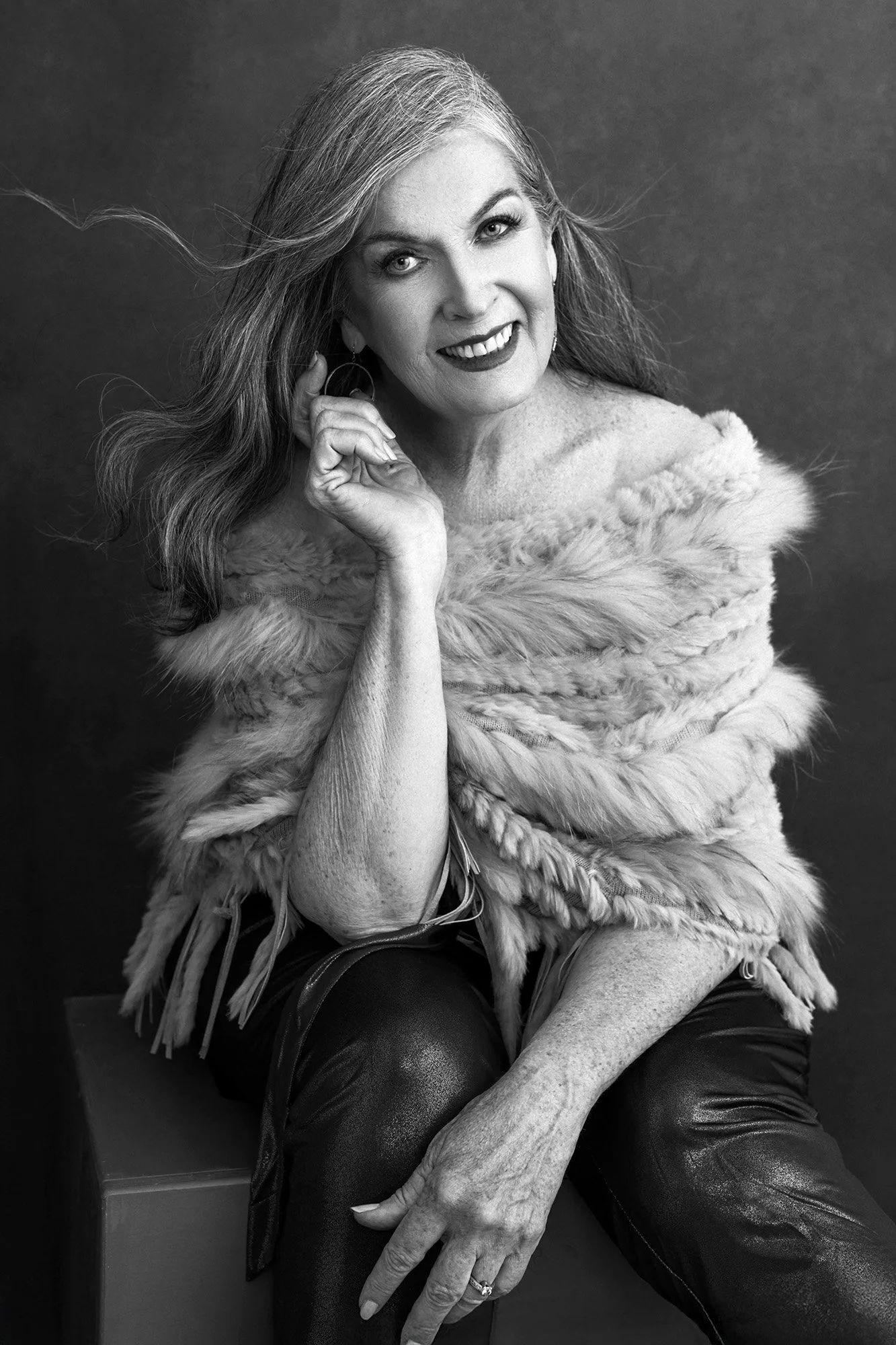 Modern women's studio photography Innsbruck — a woman over 40 in a fur wrap and leather pants, silver hair flowing freely, smiling with warmth and irresistible vivacity — 40 Over 40 Photography Project by Mayumi Acosta Photography, photo studio Innsb