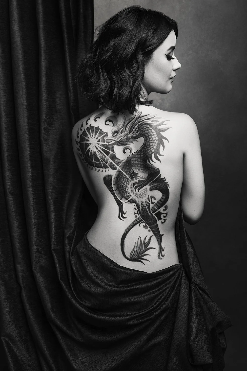 Fine art black and white portrait of a woman with full back dragon tattoo — editorial intimate photography by Mayumi Acosta, Innsbruck Austria