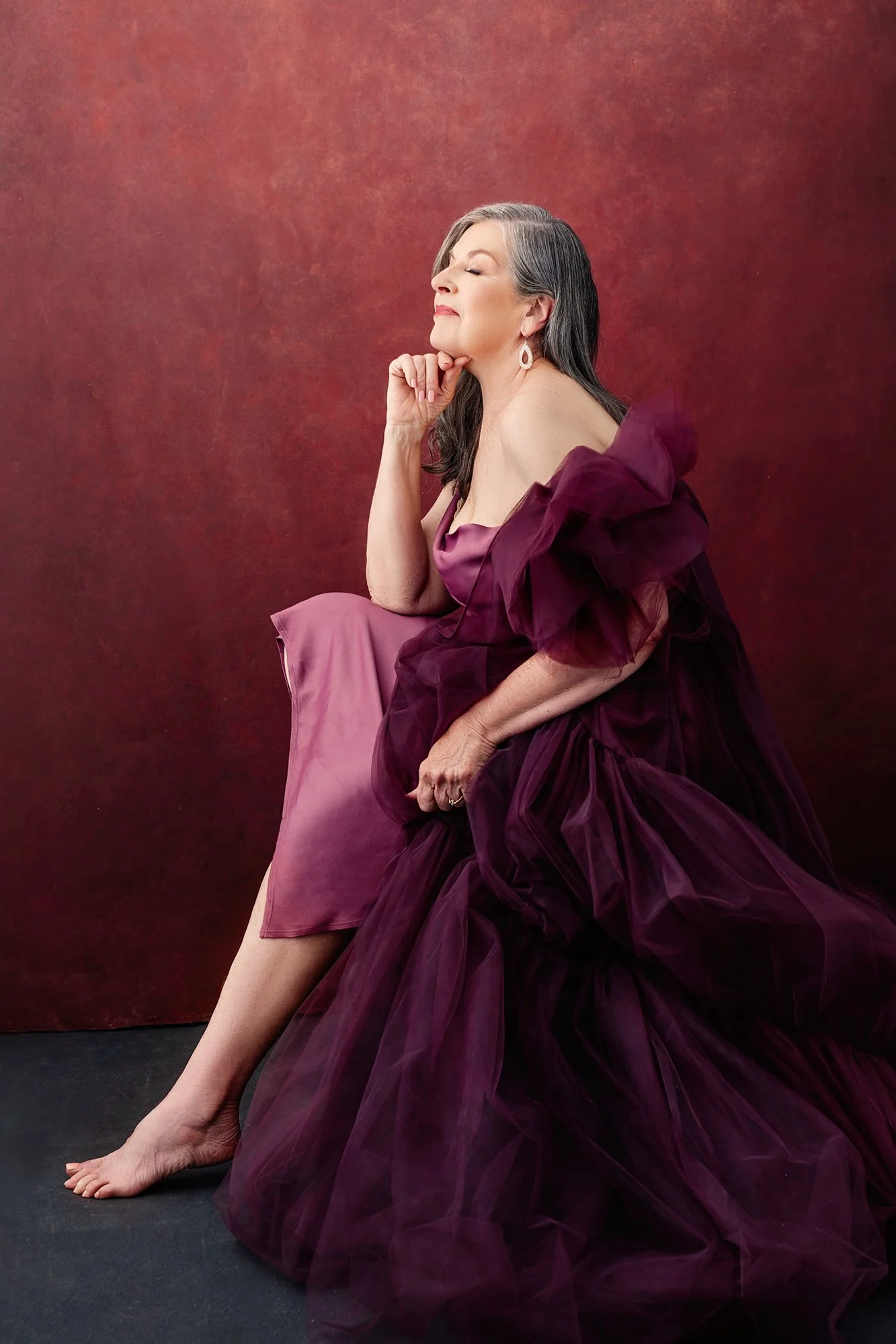Elegantes Editorial-Portrait einer Frau über 40 in einem dramatischen pflaumenfarbenen Tüllkleid, barfuß sitzend mit Hand am Kinn — Luxus Portraitfotografie für Frauen in Innsbruck, Tirol, Österreich