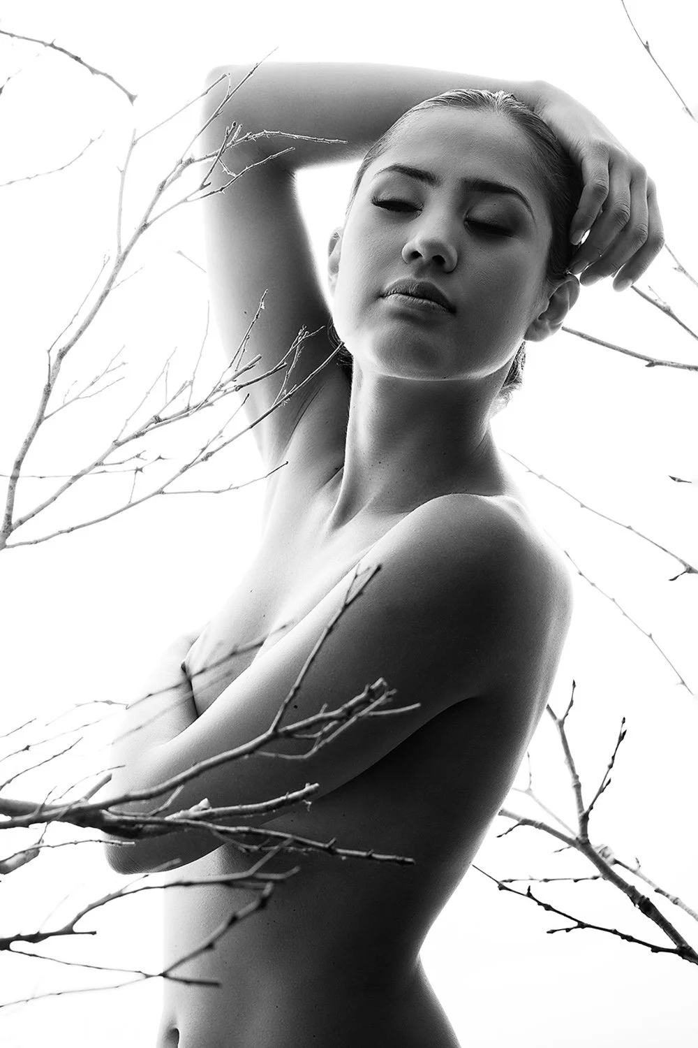 Fine art high-key black and white nude portrait of a woman among bare branches — ethereal contemporary intimate photography by Mayumi Acosta, Innsbruck Austria