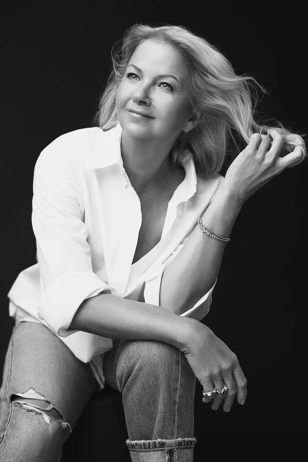 Contemporary bold portrait of a woman over 40 in a white shirt and distressed jeans, hair swept freely, gazing upward with quiet confidence — iconic woman portrait series by Mayumi Acosta Photography, photo studio Innsbruck, Tirol.