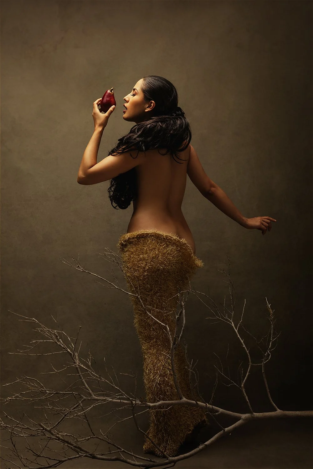 Fine art narrative nude portrait of a woman biting a pomegranate surrounded by bare branches and organic textures — mythological editorial photography by Mayumi Acosta, Innsbruck Austria