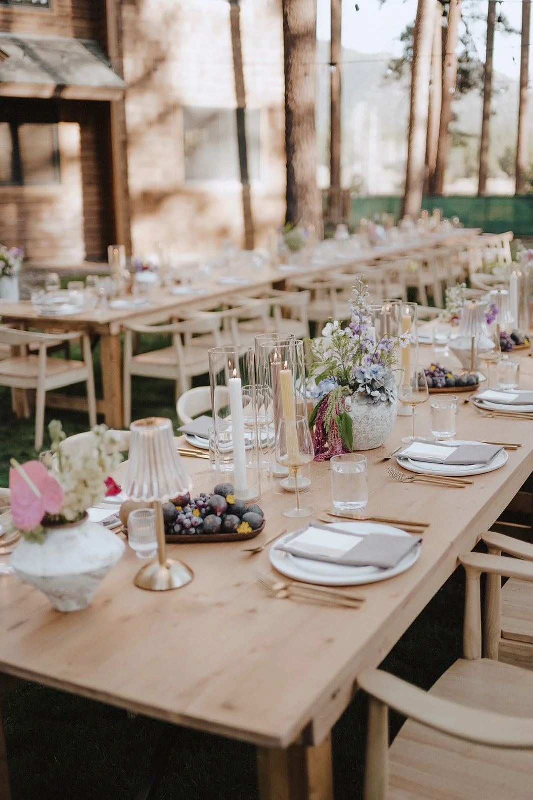 Wedding reception with light wood chairs and tables, taper candles, fruit arrangements and fluted lamps