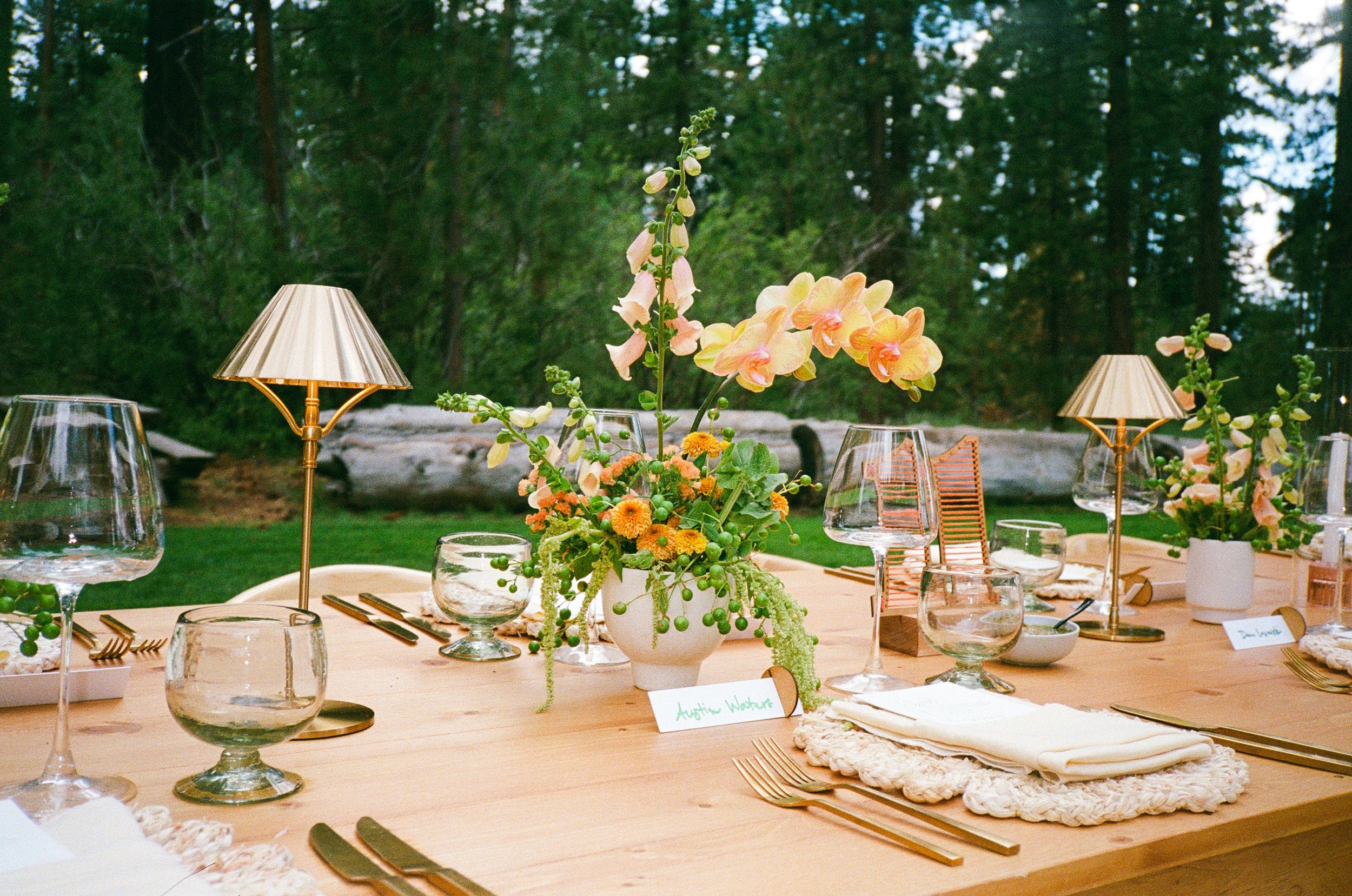 Butter yellow & pop of orange flowers for a wedding reception dinner table. Gold lamps and modern tabletop.