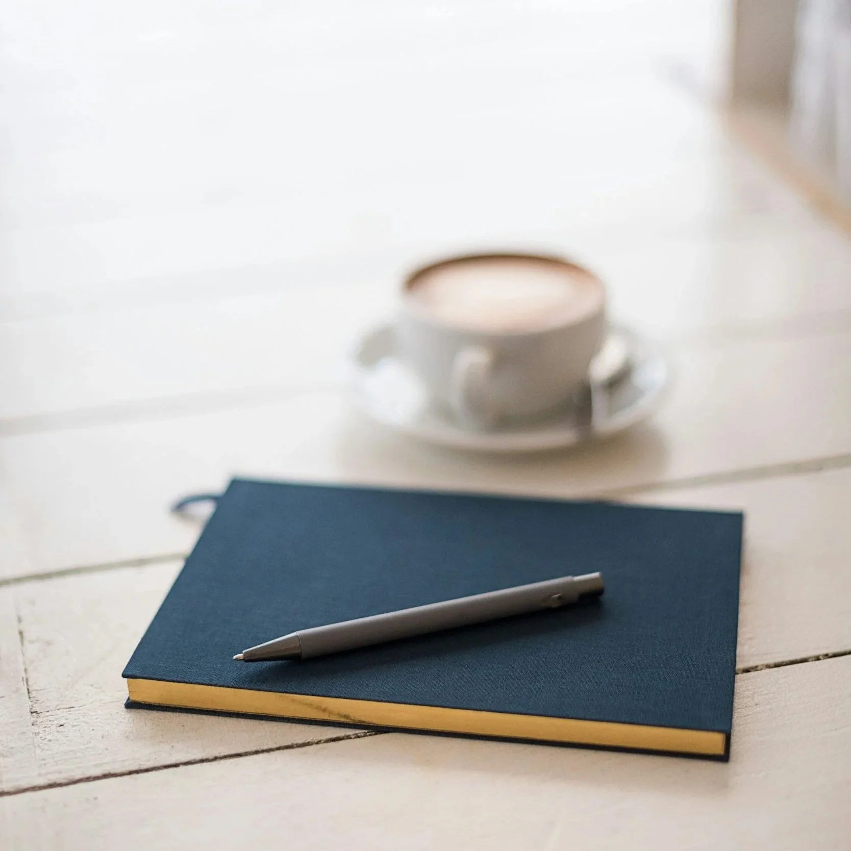 Latte in the background of a blue journal and black pen