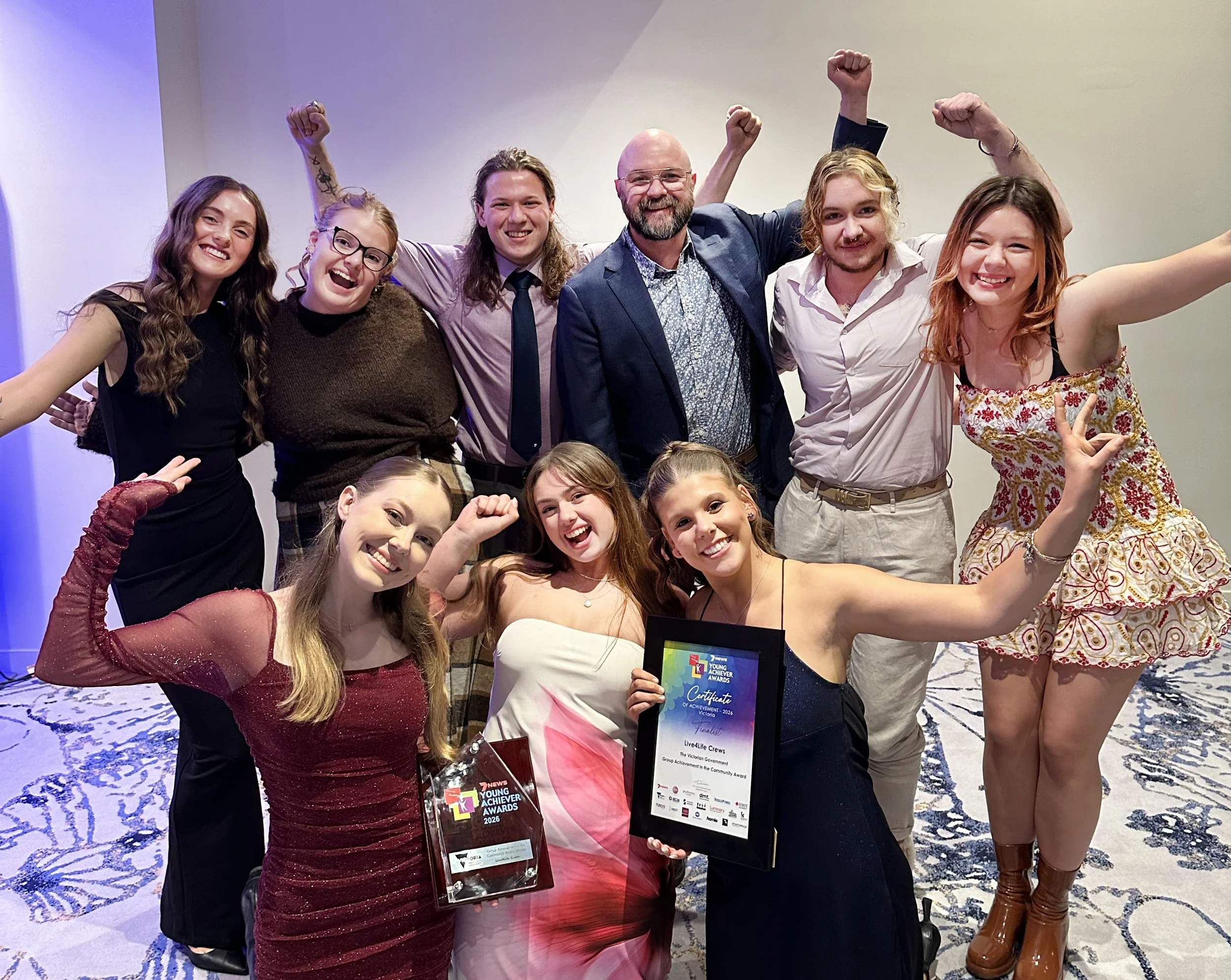 Eight young people and Live4Life CEO Jeremy Wiggins celebrate with their Young Achiever Award in the foyer of the Pullman On The Park