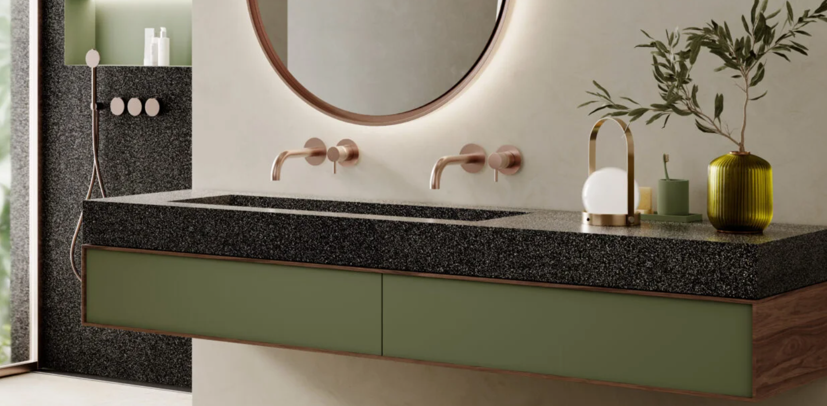 Modern bathroom vanity with a green cabinet drawer, a black speckled countertop, a round mirror, wall-mounted faucets, decorative vases, and a tree branch in a green vase.