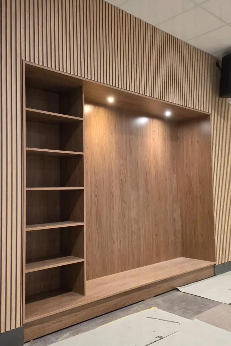 Wooden wall panel with built-in shelves and recessed lighting.