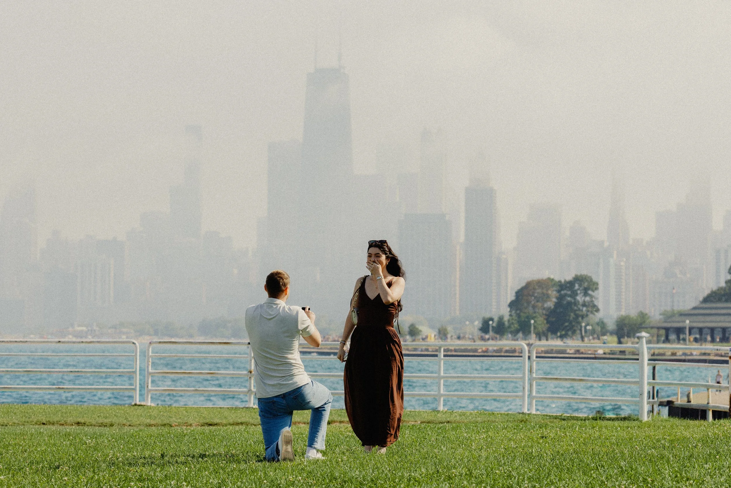 A man kneeling and taking a photo of a woman with a city skyline in the background.