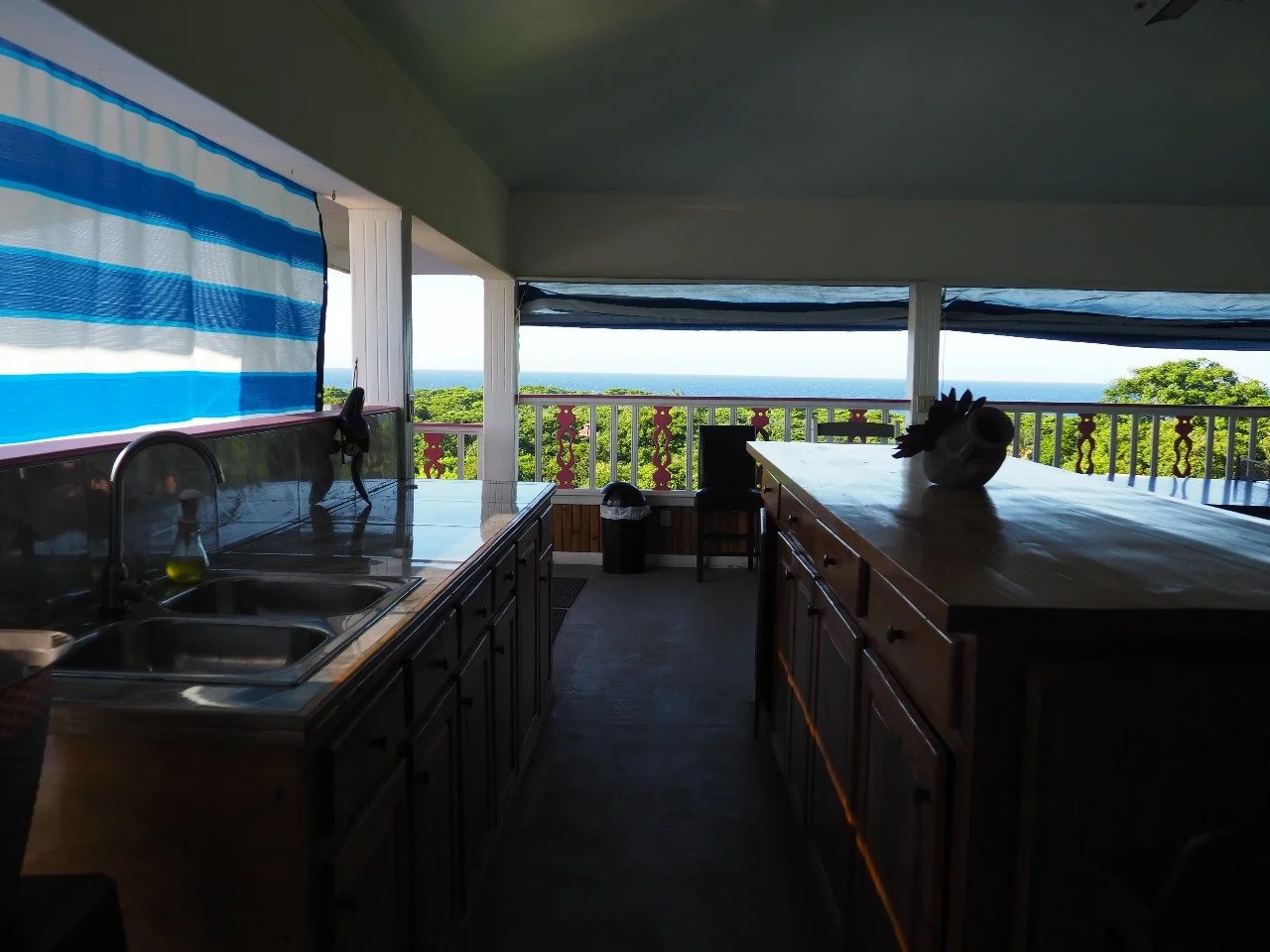 Pink Palace Utila Open-air kitchen with stainless steel sink, wooden cabinets, striped curtains, and ocean view