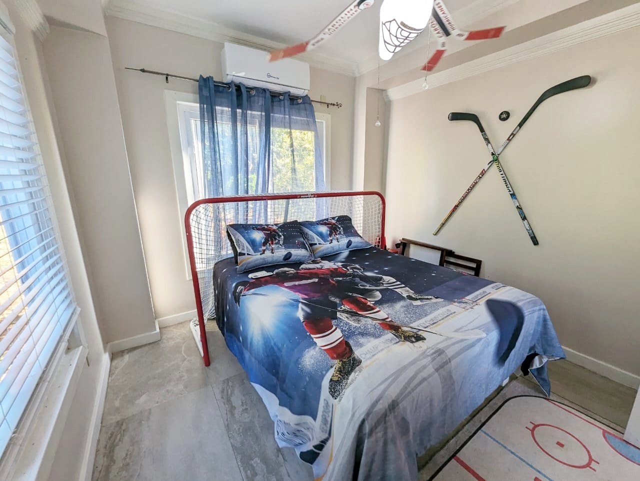 Pink Palace Utila Hockey-themed bedroom with a hockey stick headboard, crossed wall-mounted sticks, hockey bedding, and an indoor hockey goal