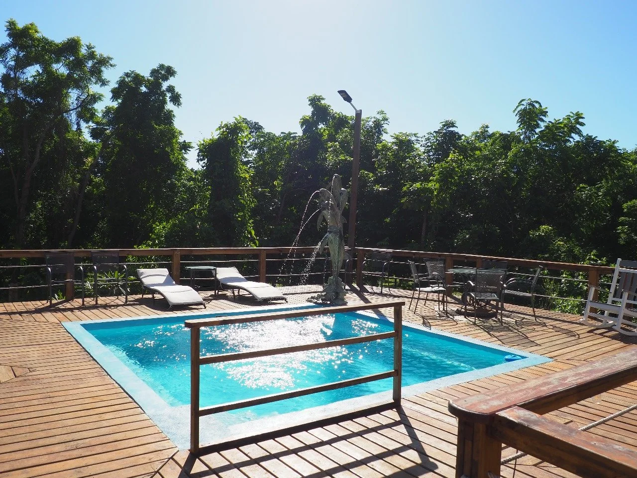 Pink Palace Utila Outdoor swimming pool with fountain on a wooden deck surrounded by lush tropical trees