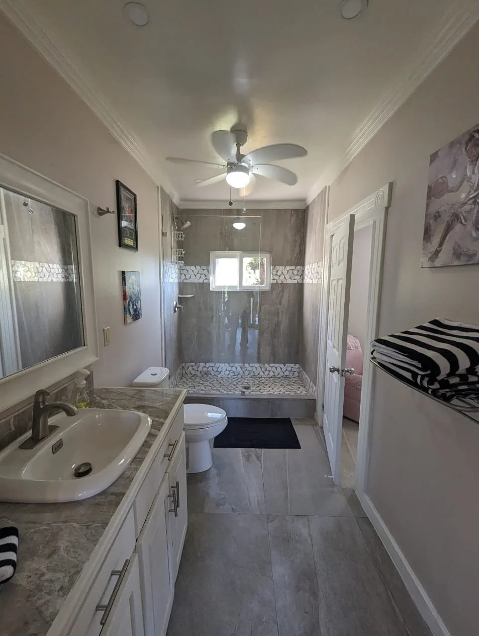 Pink Palace Utila Bright bathroom with double vanity, toilet, tiled walk-in shower, ceiling fan, and folded striped towels.