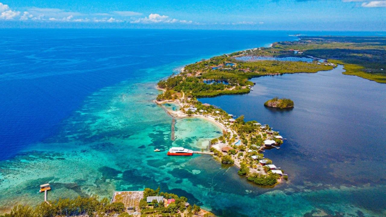 Aerial view of a tropical island with turquoise waters, sandy beaches, lush green vegetation, and overwater bungalows.