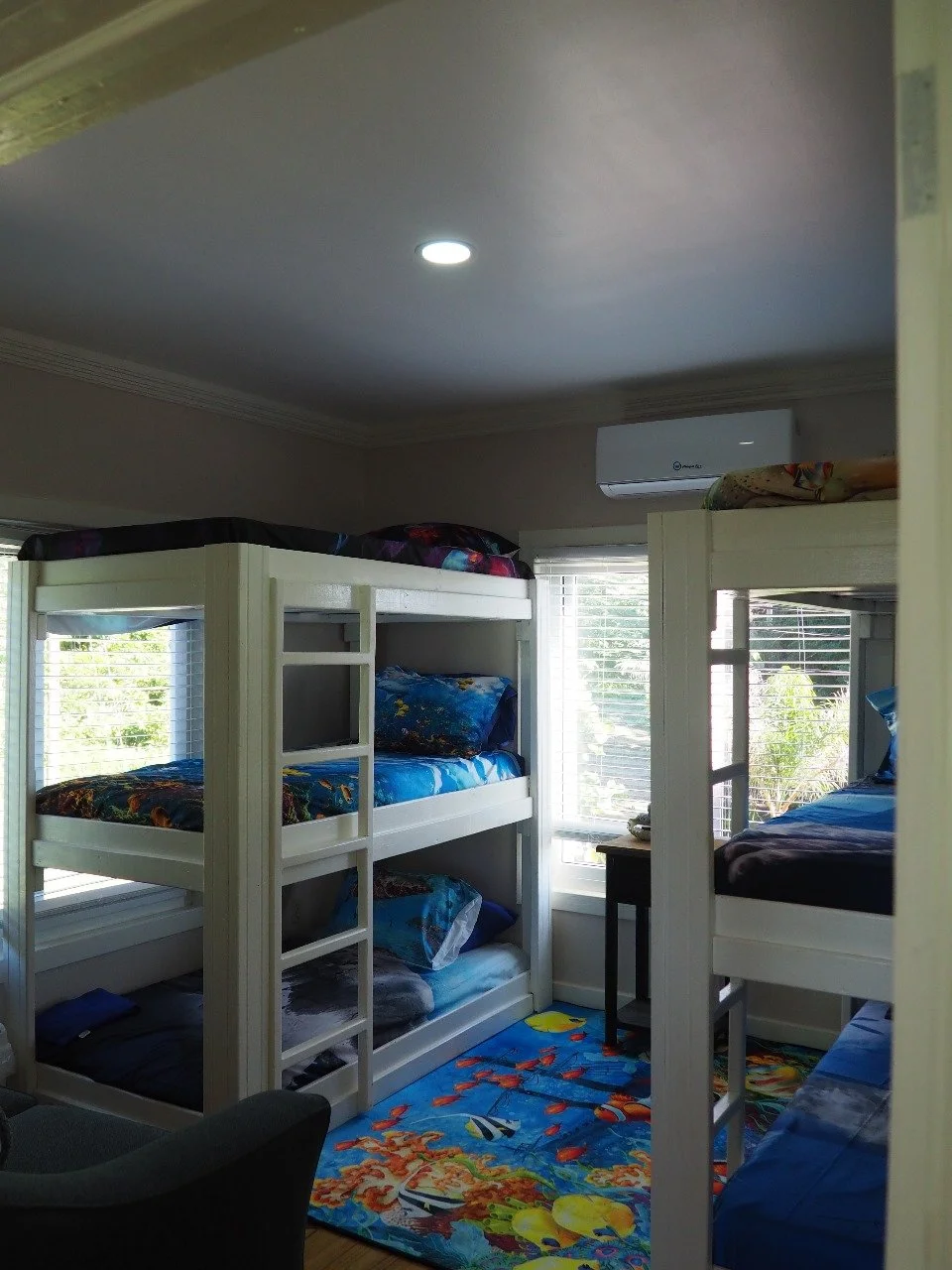 Pink Palace Utila Shared children's bedroom with white bunk beds, colorful ocean-themed bedding, large windows, and a wall-mounted air conditioner