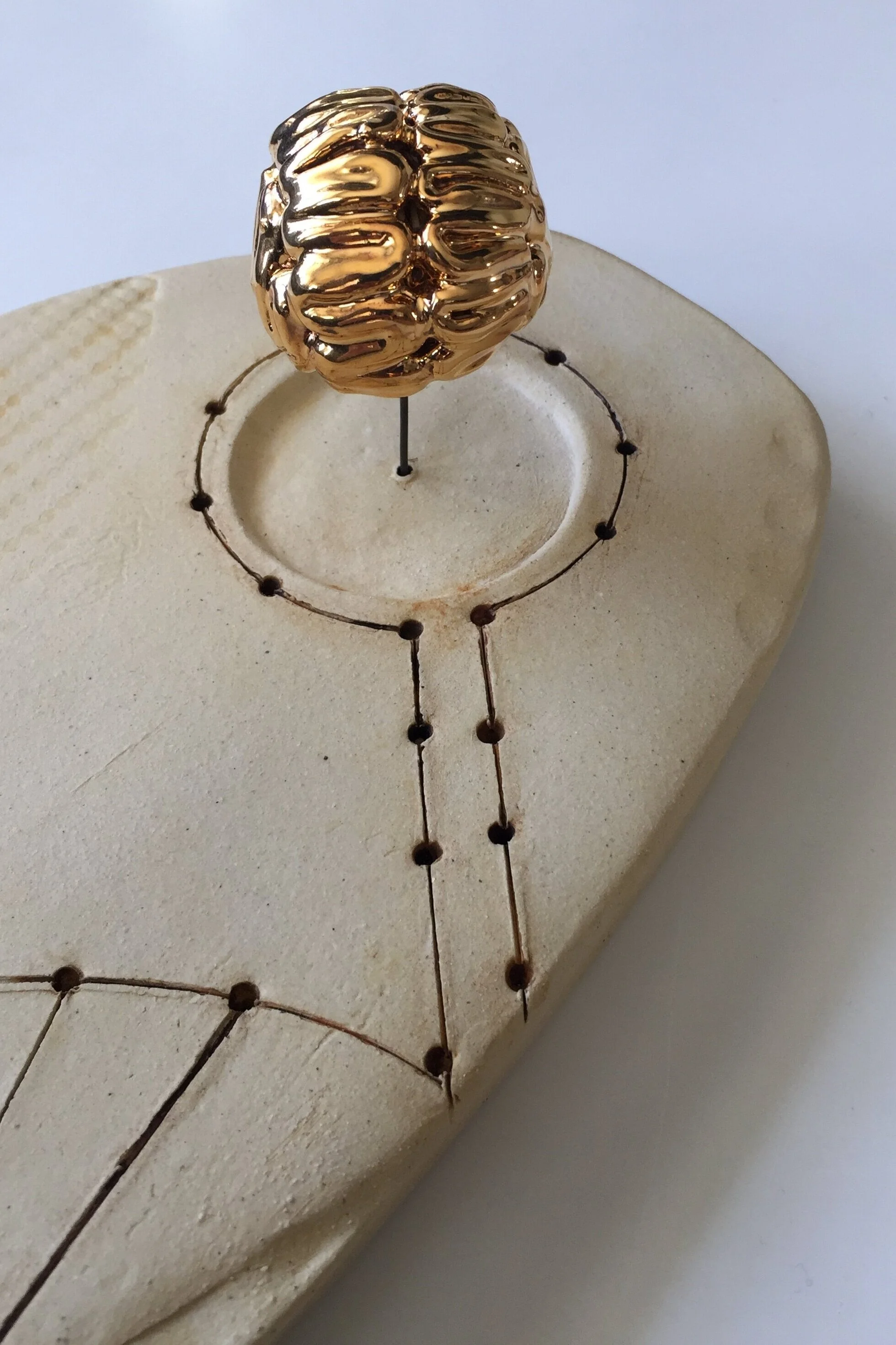 An unglazed ceramic base with a gold lustered ceramic brain projecting from the base on a metal post