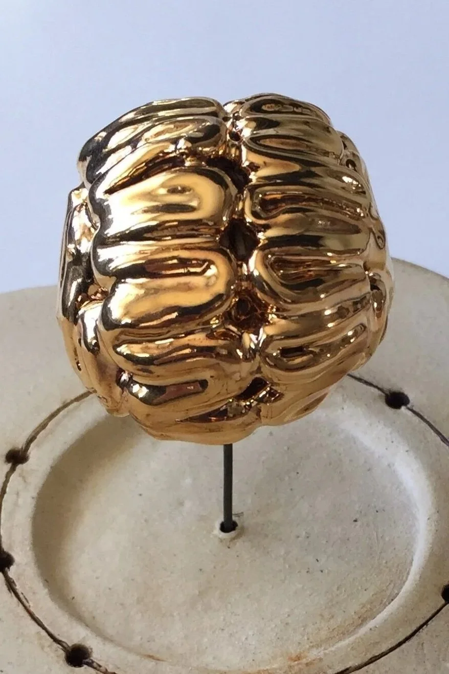 A gold-colored, reflective, sculptural object resembling a human brain mounted on a post.