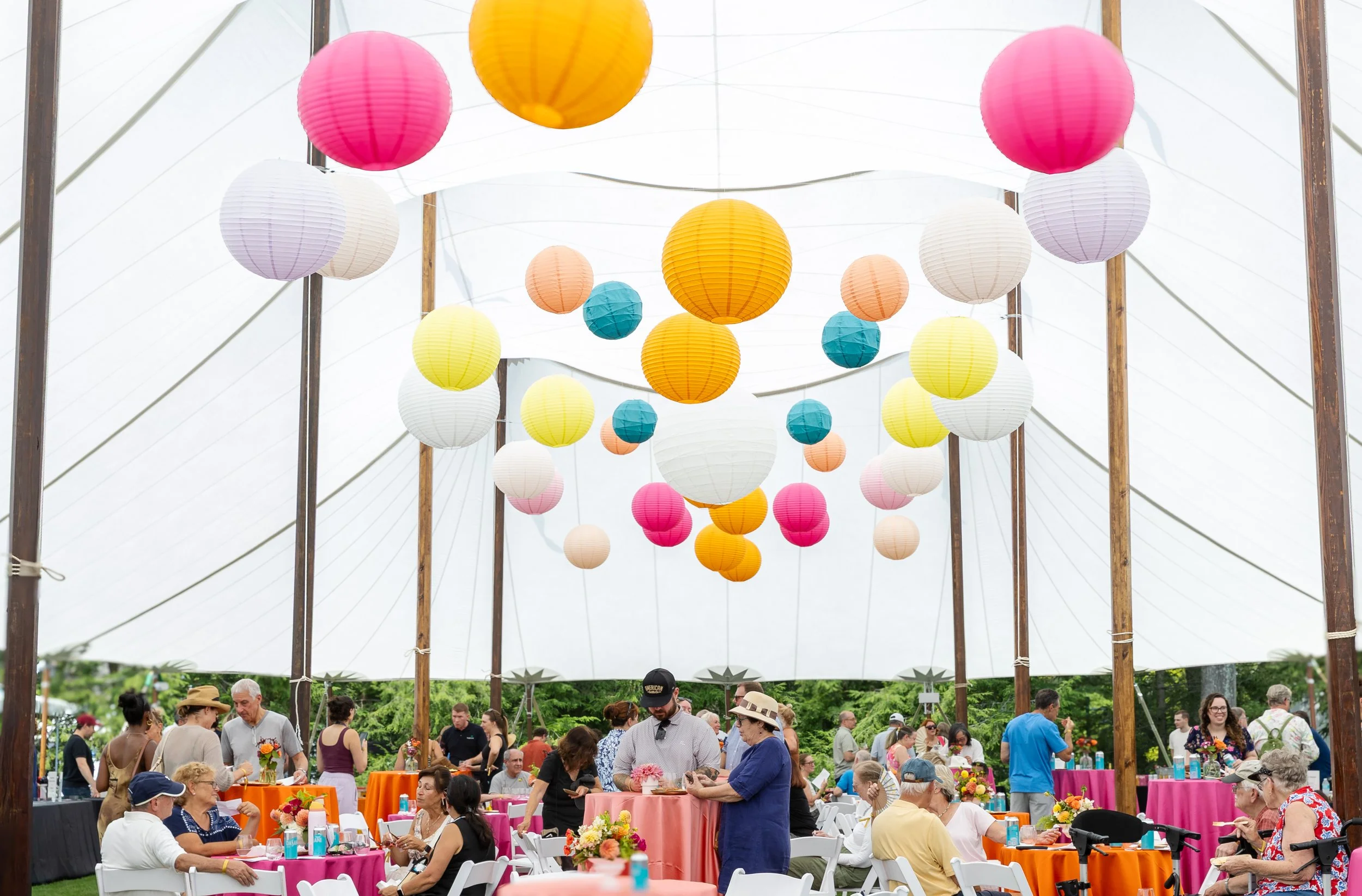 Colorful paper lanterns hanging inside a festive outdoor gathering with tables and people.